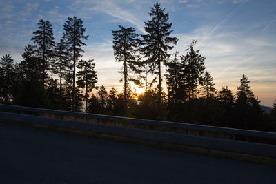 Road by trees against sky during sunset