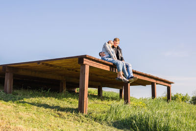 Woman sitting on bench in field against clear sky