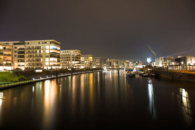 Illuminated buildings by river against sky at night