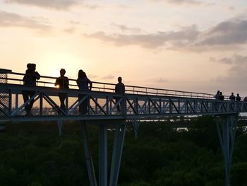 Silhouette people on footbridge against sky