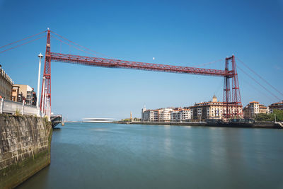 Bridge over river in city against clear blue sky