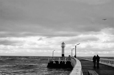 People standing on lighthouse by sea against sky