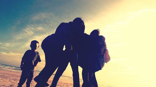 Silhouette people at beach against sky during sunset