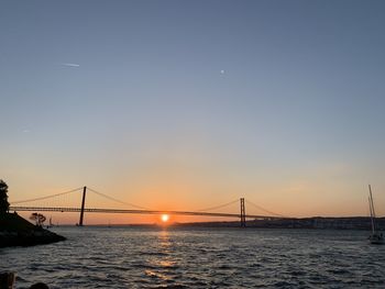 Suspension bridge over sea against sky during sunset