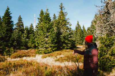 Side view of man standing by trees in forest against sky