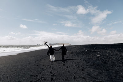 Friends riding horse on beach against sky