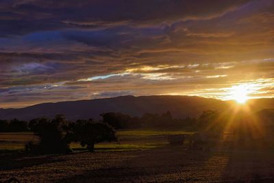 Scenic view of landscape against dramatic sky at sunset