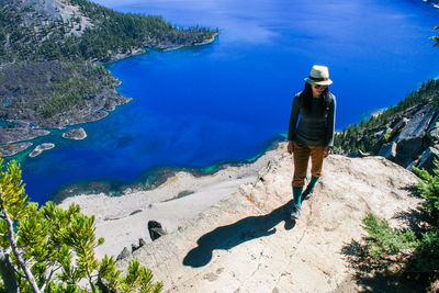 High angle view of young woman standing on cliff by crater lake