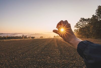 Optical illusion of man holding sun on field against sky during sunset