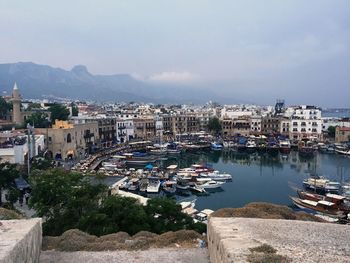 Boats moored at harbor by buildings against cloudy sky