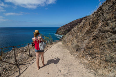 Rear view of woman using phone while standing against sea