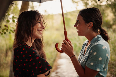 Side view of lesbian couple laughing while standing under umbrella
