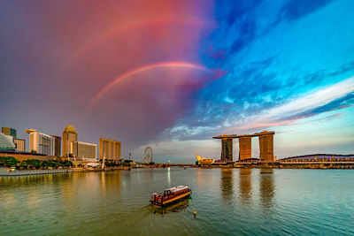 Scenic view of rainbow over river by buildings in city against sky