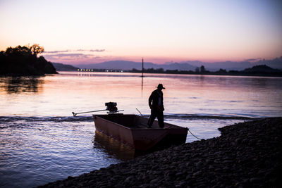 Silhouette man fishing on beach against sky during sunset