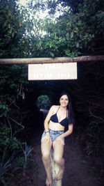 Portrait of young woman standing by tree in forest