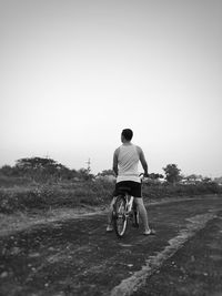 Rear view of man with bicycle standing on road against clear sky