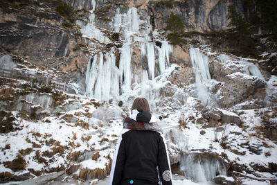 Rear view of woman looking at waterfall during winter