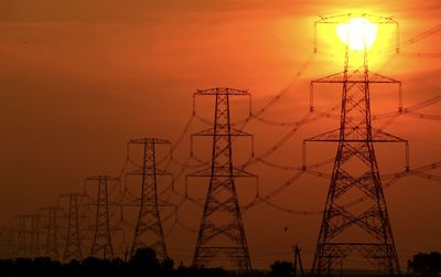 Low angle view of silhouette electricity pylon against sky during sunset