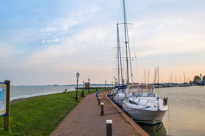 Sailboats moored at harbor against sky during sunset