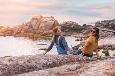 People sitting on rock by sea against sky