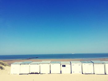 Beach huts on shore against clear blue sky