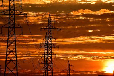 Low angle view of silhouette electricity pylon against dramatic sky