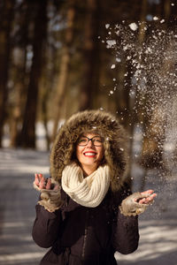 Portrait of young woman throwing snow on field