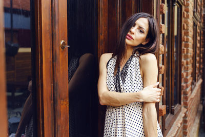 Young woman looking away while standing on door