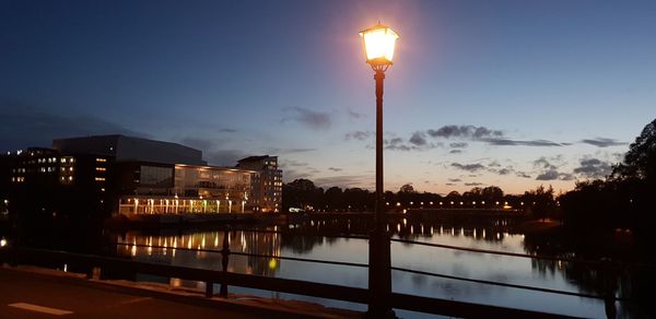 Illuminated street lights by lake against sky at night