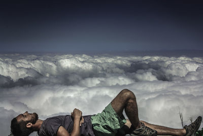 Side view of man lying on cliff by cloudy sky