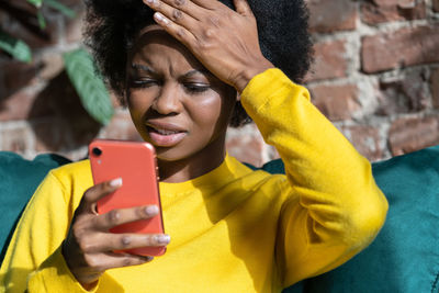 Thoughtful woman using smart phone while sitting home