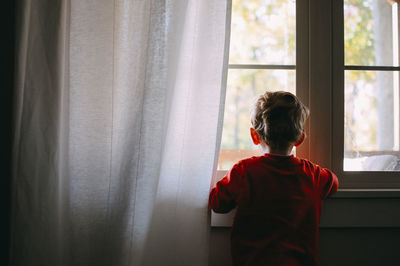 Rear view of baby boy looking through window at home