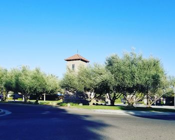 Trees by road against clear blue sky