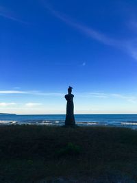 Statue on beach against blue sky