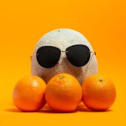 Close-up of fruits and sunglasses against orange background