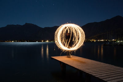 Ferris wheel by lake against sky at night