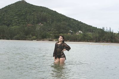 Portrait of smiling woman in swimwear standing amidst lake against mountain