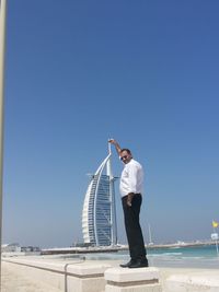 Rear view of man standing by sea against clear blue sky