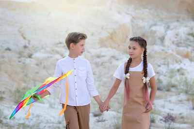 A boy and girl walk holding hands, the boy carries a kite.