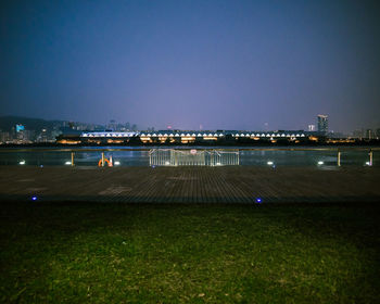 Illuminated city by river against clear sky at night