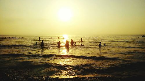 Silhouette people enjoying in sea against sky during sunset