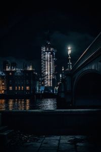 Illuminated buildings by river against sky at night