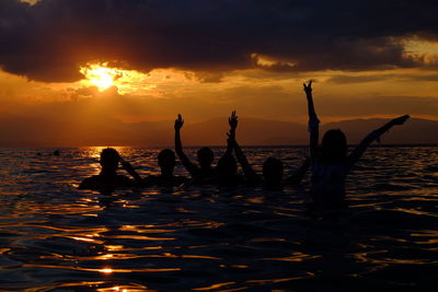 Silhouette people by sea against sky during sunset