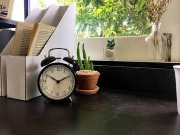 Close-up of alarm clock by potted plant on table at home