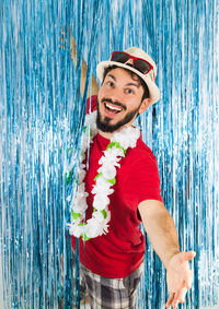 Portrait of cheerful man with arms outstretched wearing floral garland and hat