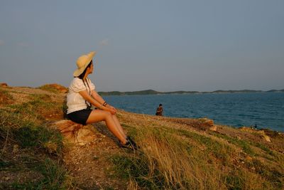 Woman on grass by sea against sky