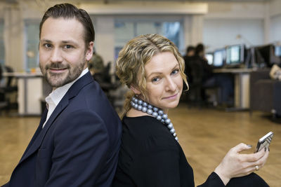 Portrait of confident businessman and businesswoman sitting back to back in office