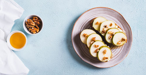 Pieces of pear, ricotta, honey and nuts on rye bruschettas on a plate top view web banner