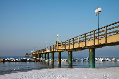 Footbridge at calm sea against blue sky