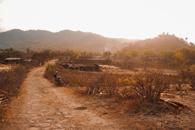 Dirt road passing through field against clear sky